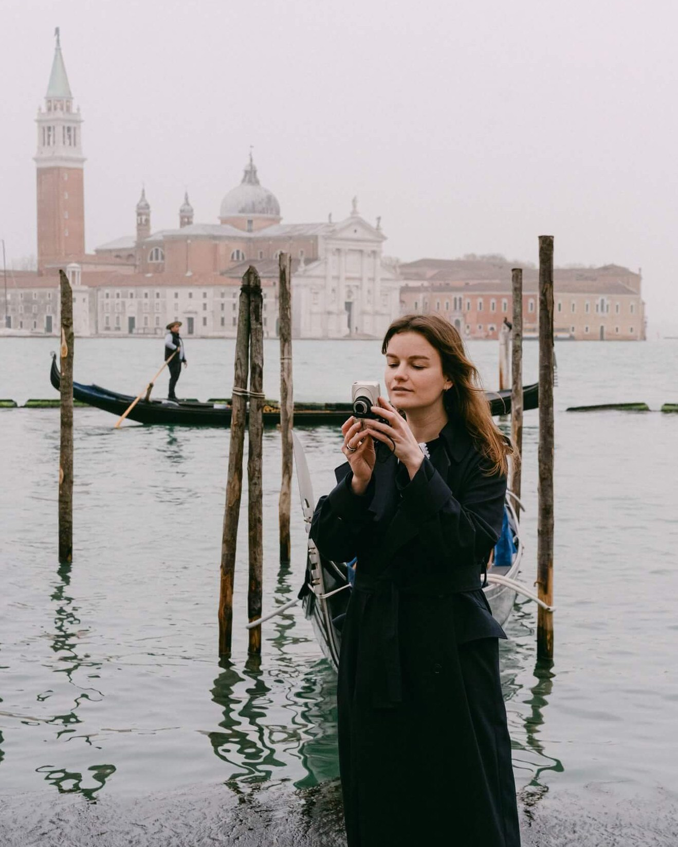 Inna Zaytseva, destination wedding photographer, standing by the Venice waterfront with gondolas and San Giorgio Maggiore in the background