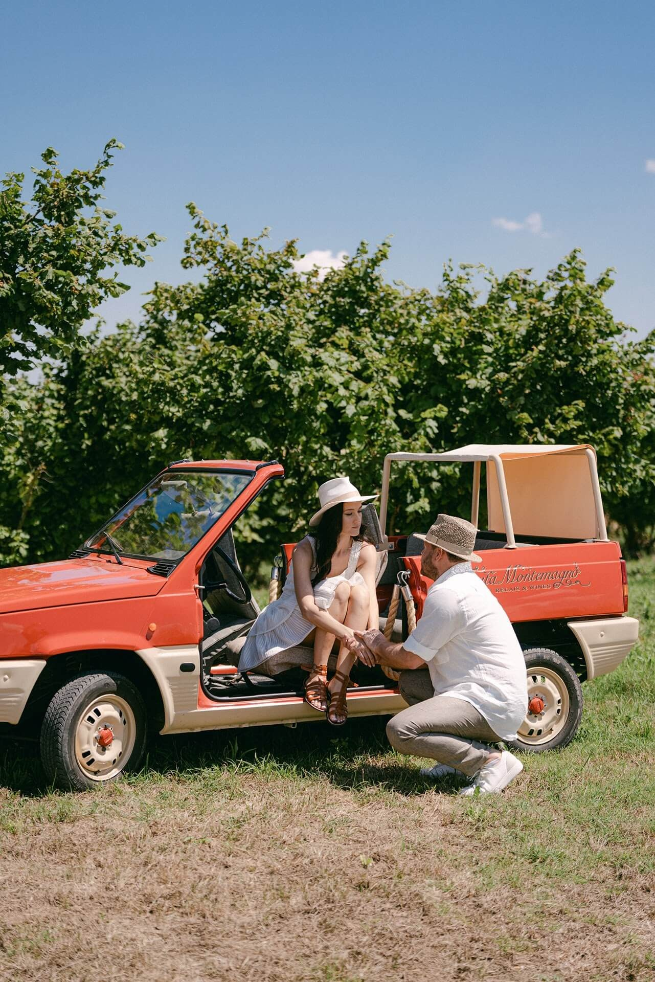 Couple beside a vintage red car among Langhe vineyards during a summer wedding shoot in Piedmont