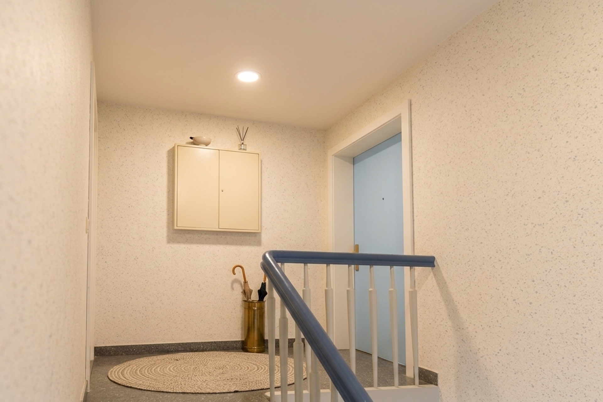 KI-gestalteter Flureingang: Treppenhaus-Ansicht mit virtueller Möblierung, Jute-Teppich, Vintage-Schirmständer und pastellblauer Tür. Fotoservice von jade-visual.