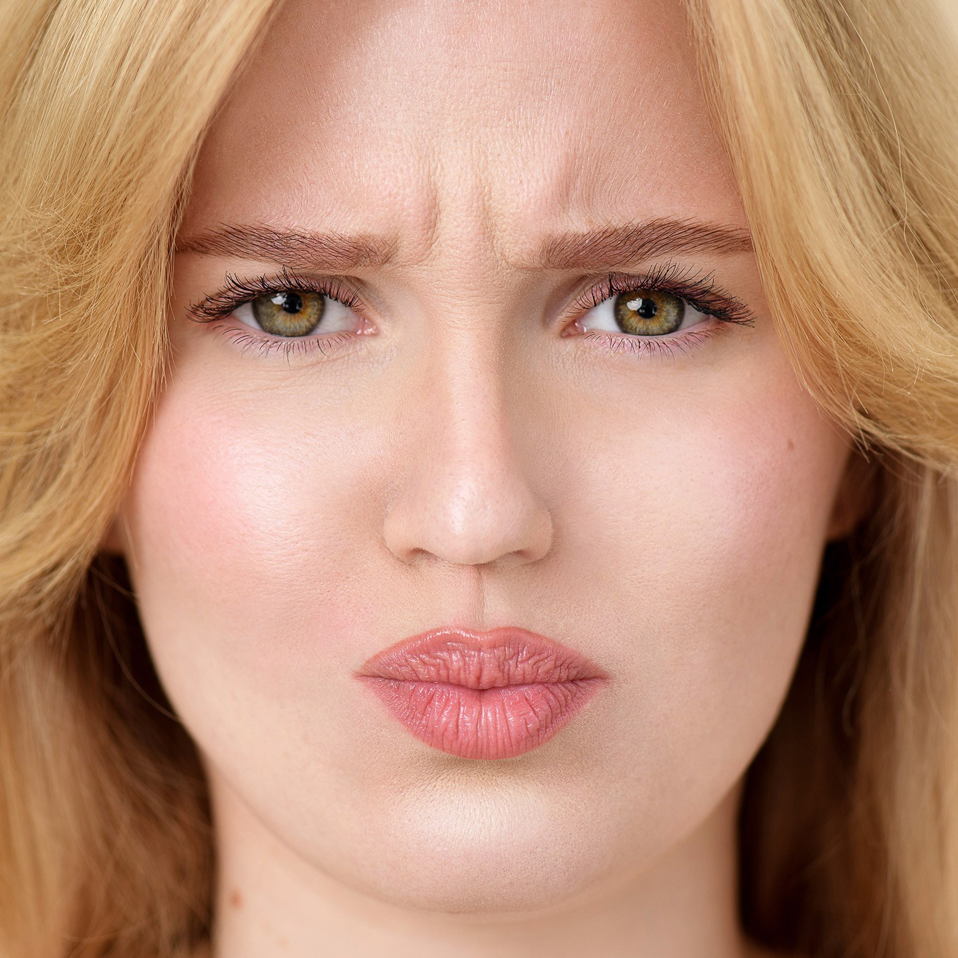 Close-up beauty portrait of a blonde woman with natural makeup and expressive facial features, photographed in a professional studio setting