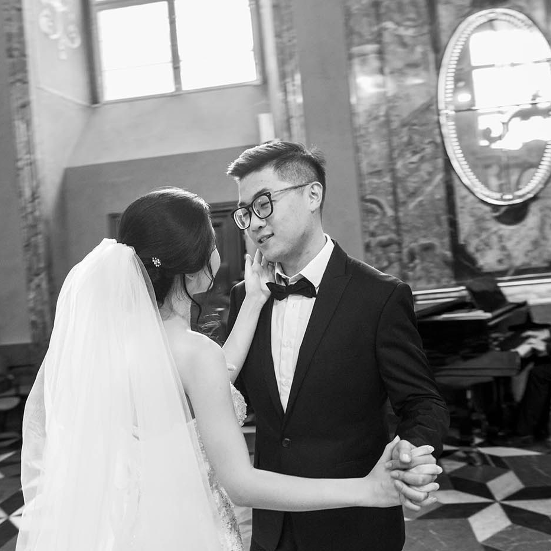 As the newlyweds dance while the pianist plays, the bride lovingly strokes the face of her groom during their Klementinum Mirror Chapel wedding celebration in Prague