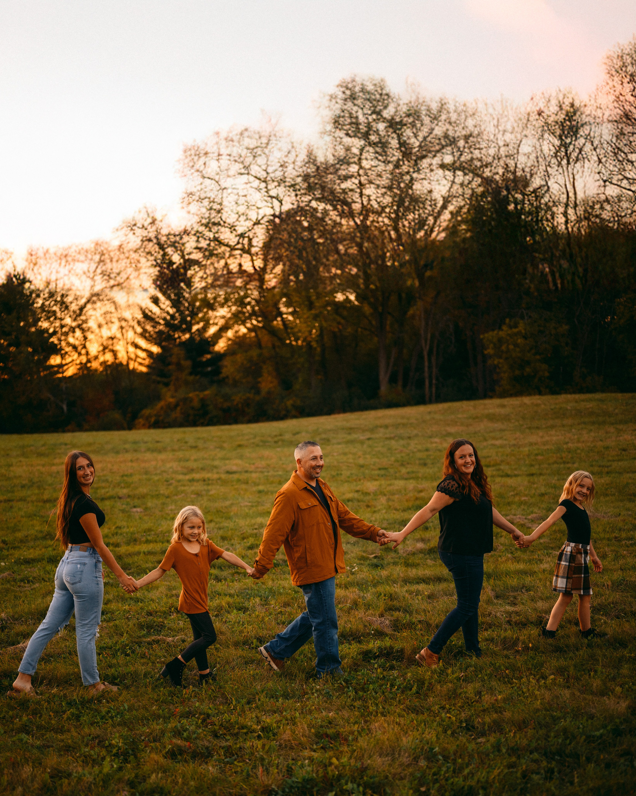 Sunset family portrait session in Green Bay, Wisconsin. Natural light photography capturing joyful moments of families walking together in a golden hour setting. https://www.dodged-magazine.com/artists-portfolios-and-bios/ilia-bordiugov?rq=Bordiugov