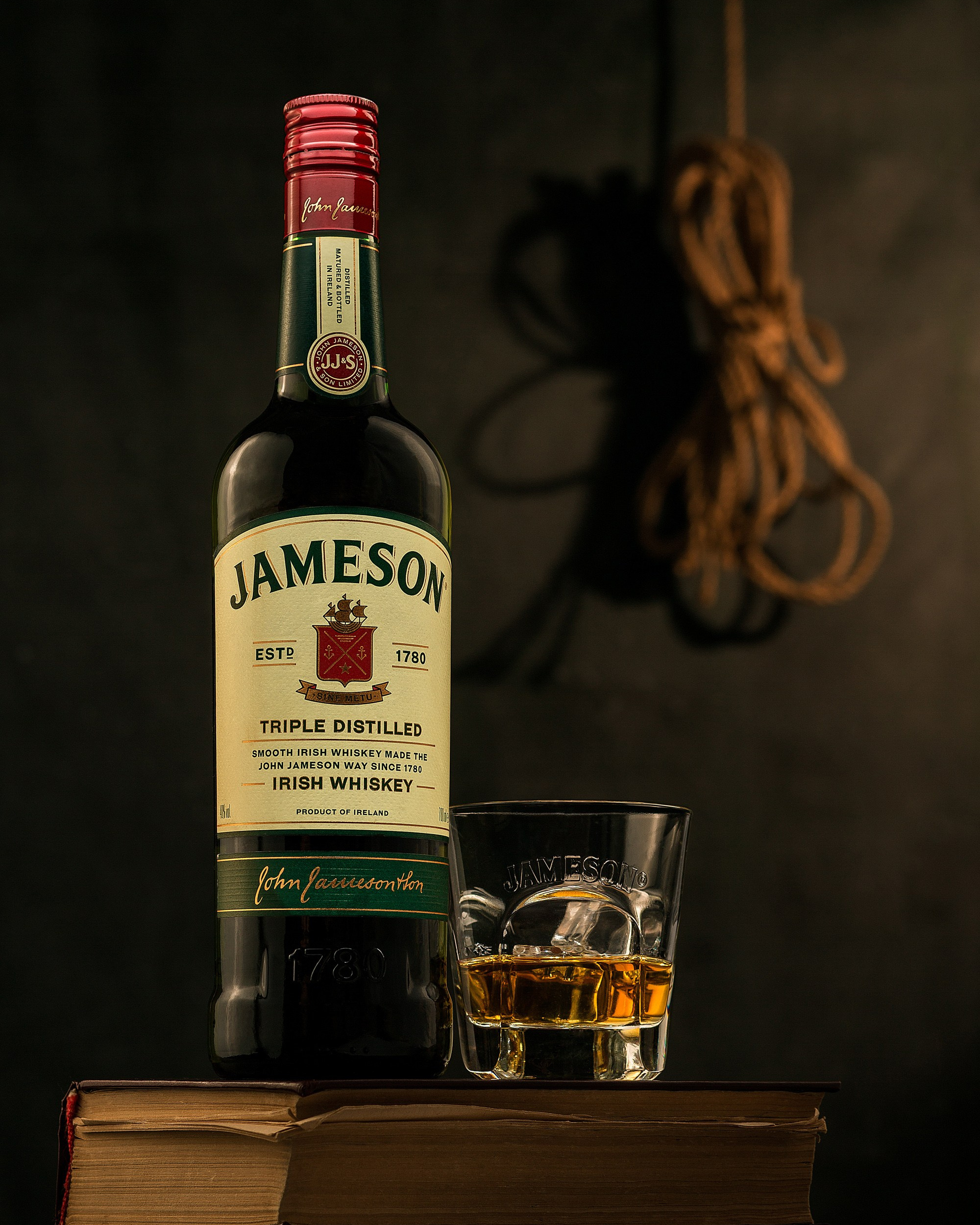 Tünd işıqda köhnə kitablar üzərində Jameson viski şüşəsi və stəkan