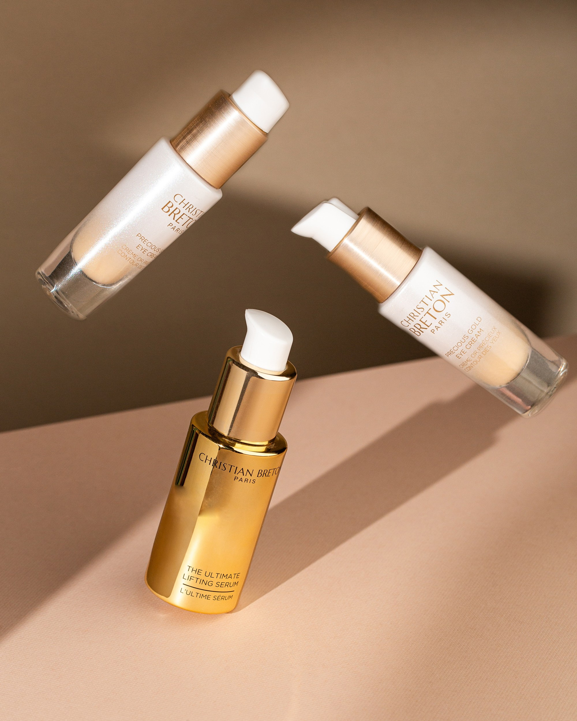 Christian Breton Paris kosmetik məhsulları – iki ədəd Precious Gold Eye Cream şüşəsi havada, ortada isə qızılı The Ultimate Lifting Serum şüşəsi minimalistik fon üzərində yerləşdirilib.