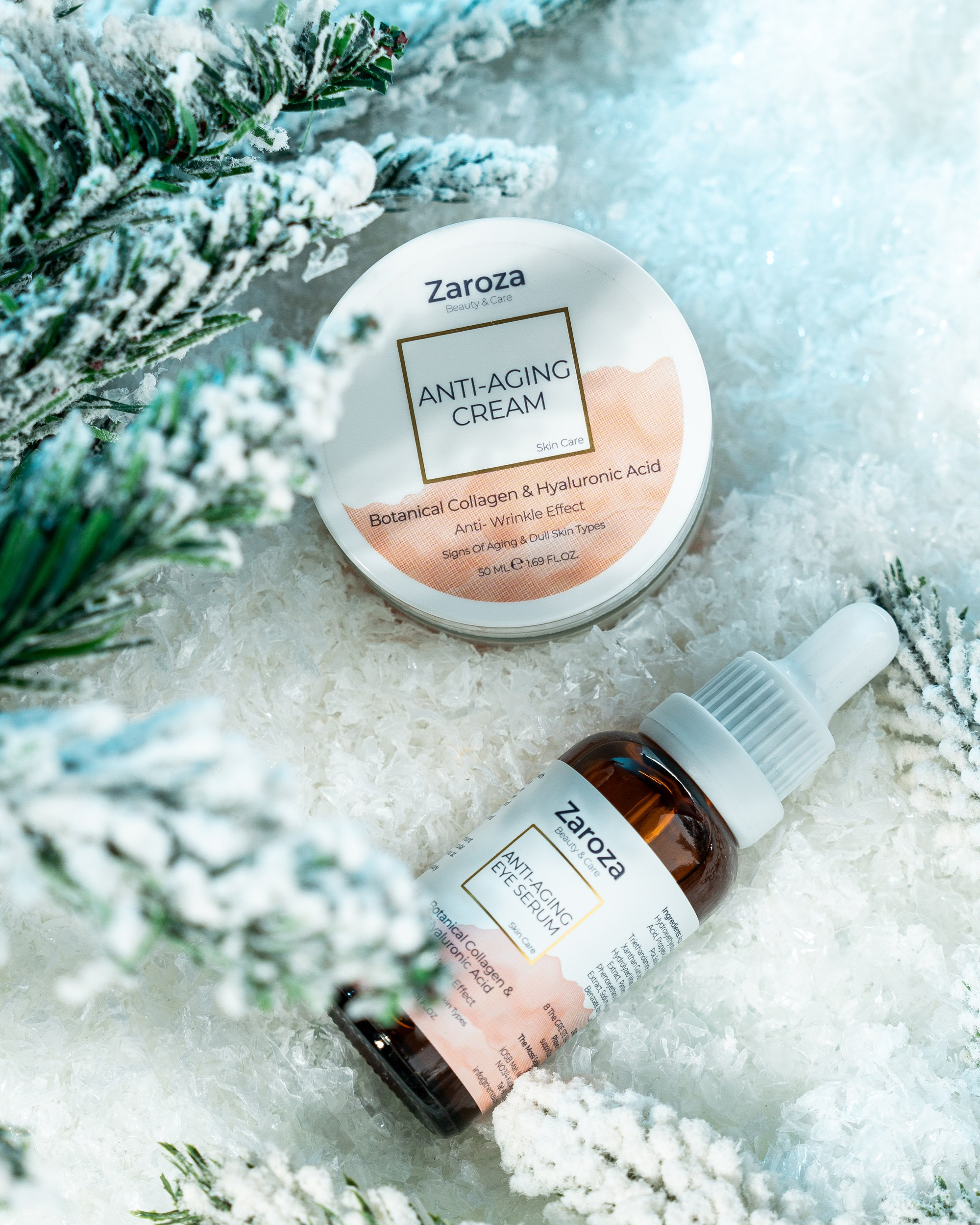 Qar və saxta şam ağacı budaqları ilə bəzədilmiş mühitdə, qocalma əleyhinə (Anti-Aging) Zaroza seriyası: "Anti-Aging Cream" yazılı ağ qab və "Anti-Aging Eye Serum" yazılı şüşə damcı başlıqlı butulka.
