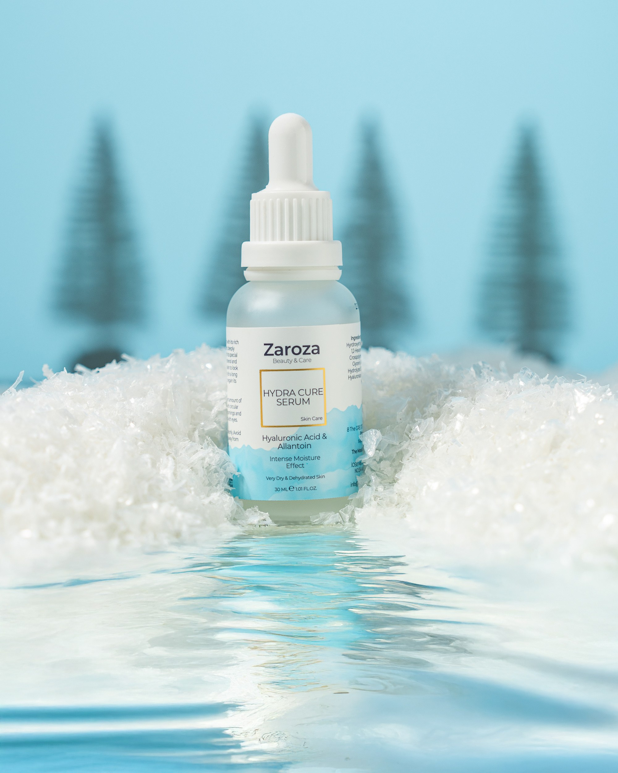 Mavi fonda, qar yığını və bulanıq şam ağacı siluetləri arasında suyun səthində dayanan, "Zaroza Hydra Cure Serum Hyaluronic Acid & Niacinamide" yazısı olan damcı başlıqlı butulka.