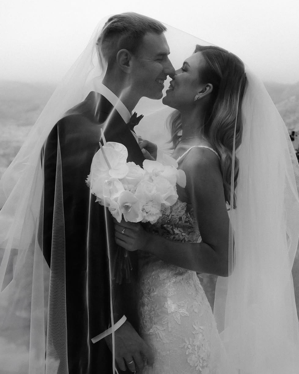 A bride and groom sitting on a boat, celebrating with champagne as the bride raises her glass. The marina with boats and reflections on the water creates a romantic backdrop.