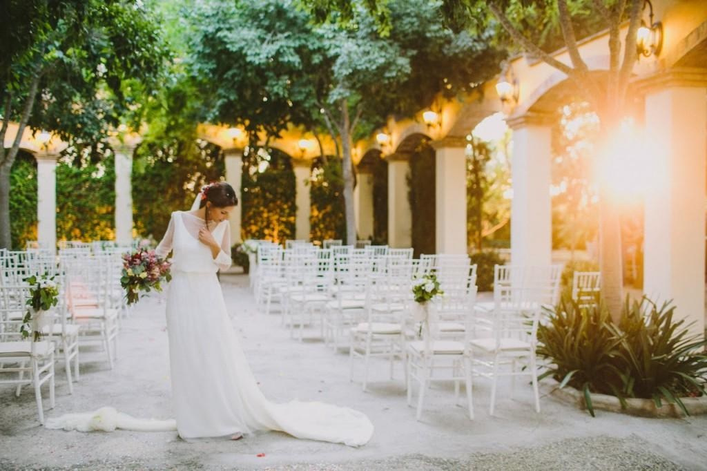 Bride holding a bouquet in Masía Xamandreu’s sunlit ceremony courtyard, surrounded by white chairs and arches.