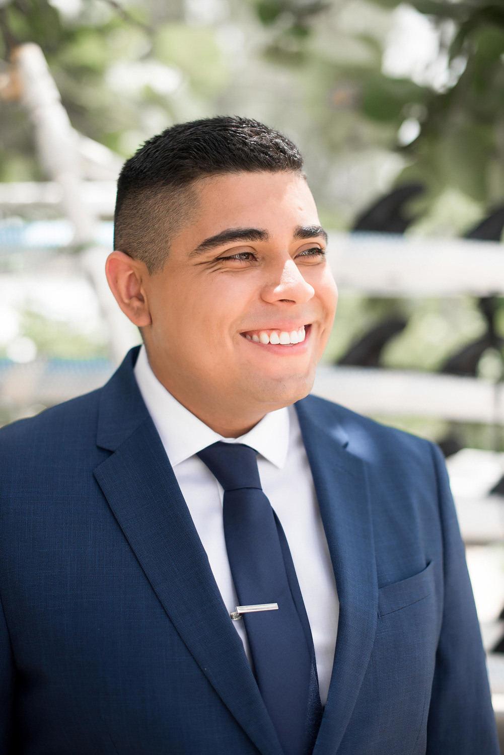 Жених улыбается невесте, он одет в классический костюм с галстуком.