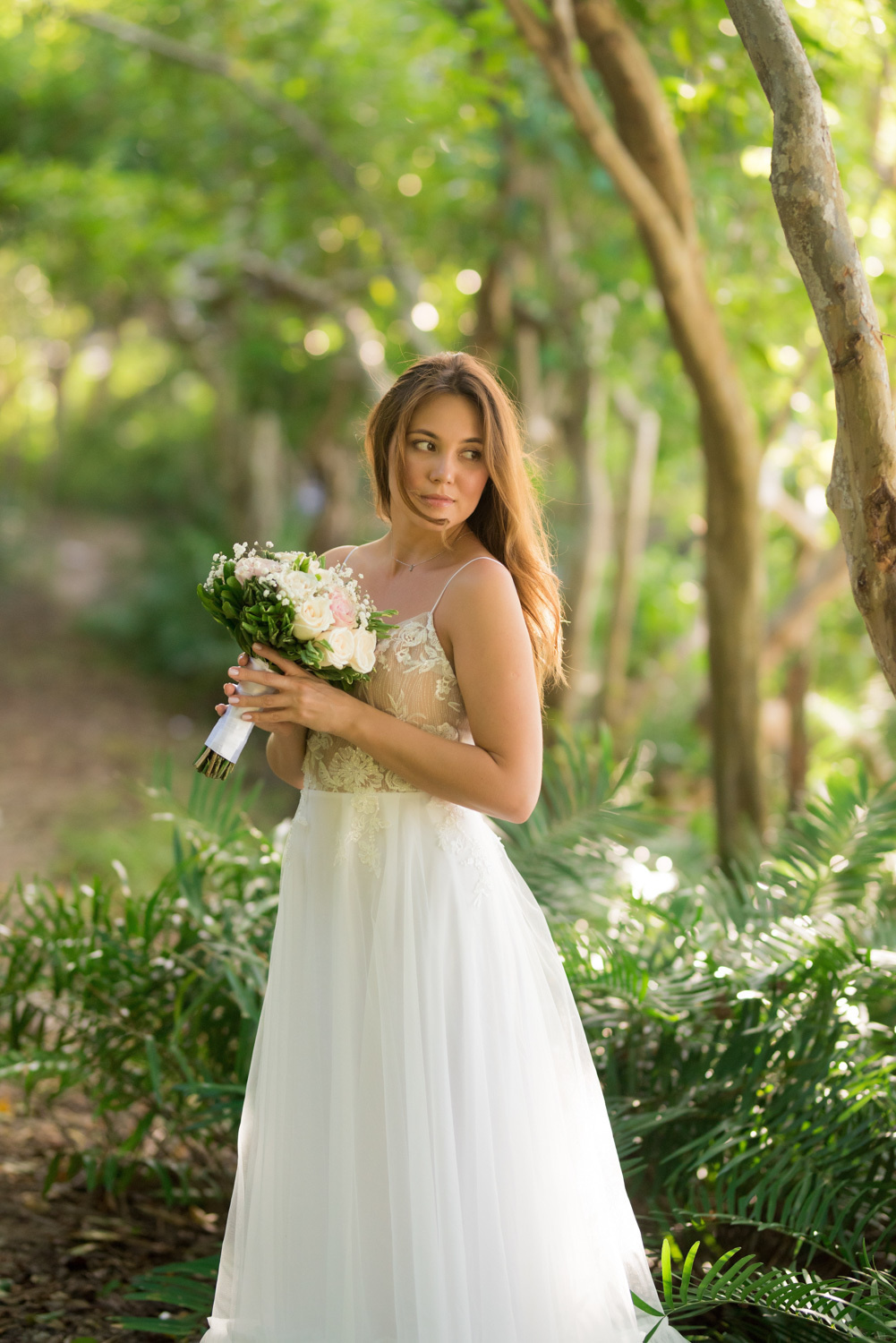 The bride looks into the camera to the photographer, she is holding a bridal bouquet of fresh flowers, her hair is fluffed out, and she is wearing a white wedding dress.