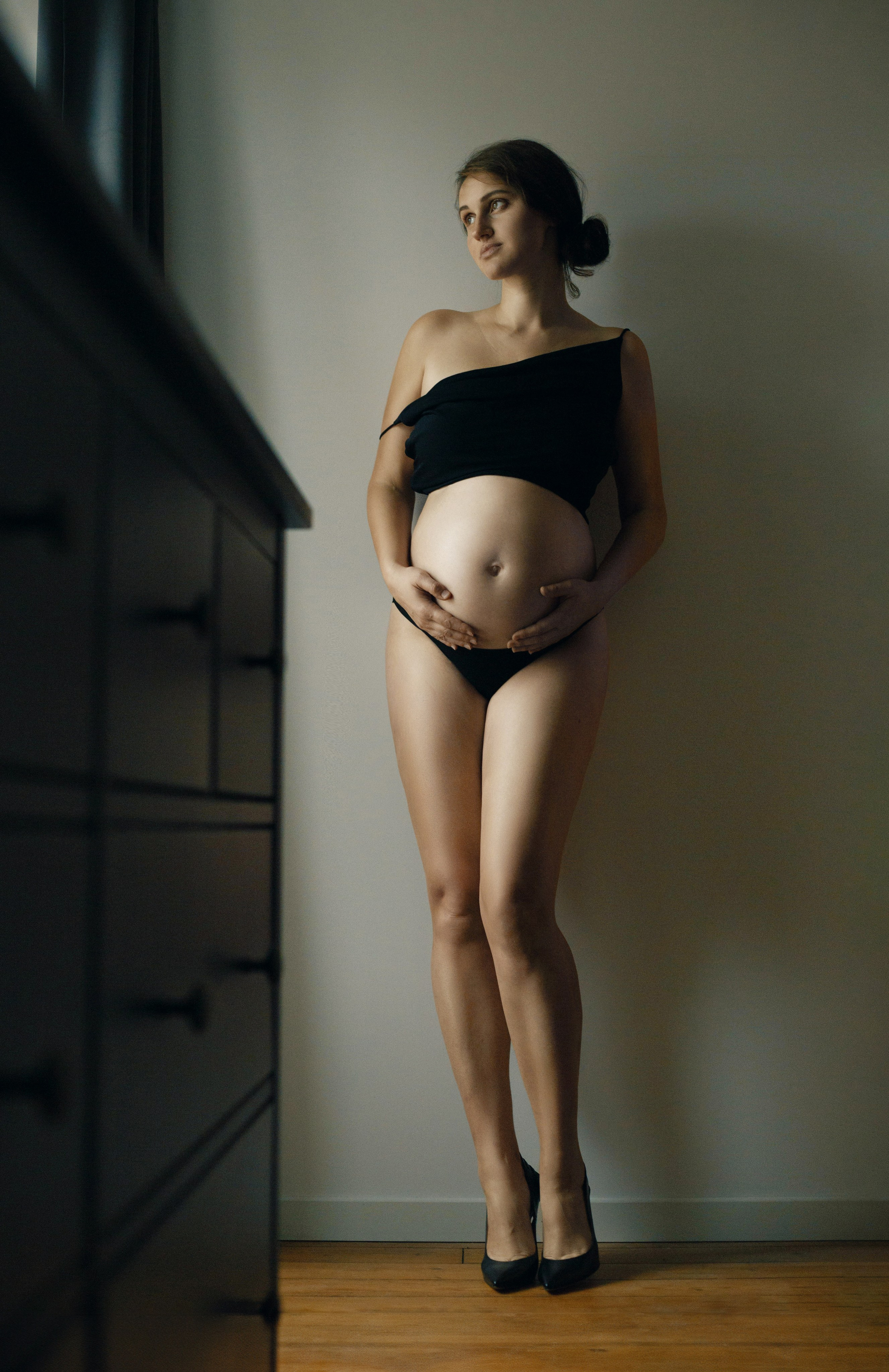 Portrait élégant de femme enceinte debout en lingerie noire, lumière douce et composition minimaliste