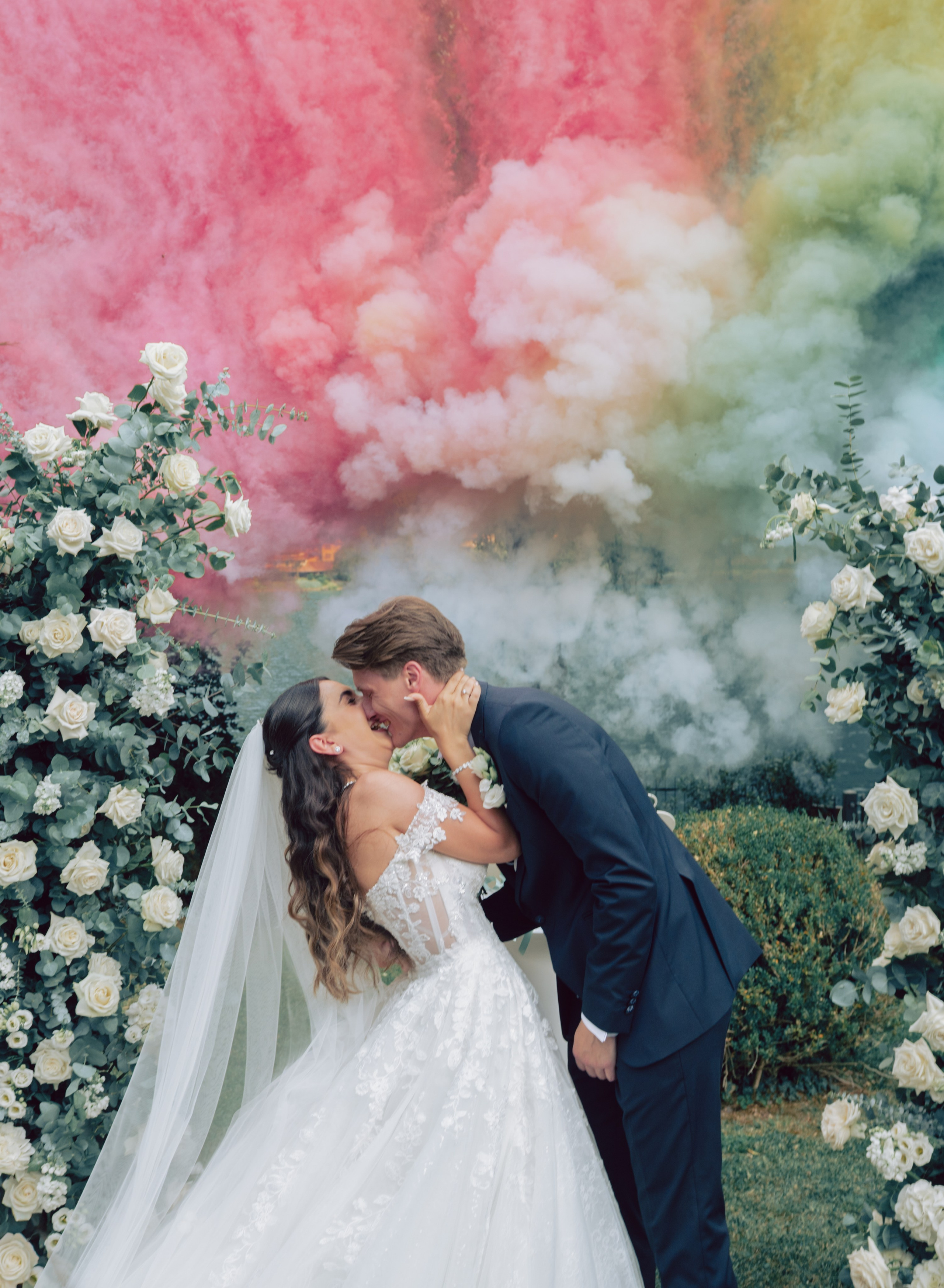 Bride and groom kissing beneath colorful smoke bombs at an Italian destination wedding. Destination wedding photographer in Italy