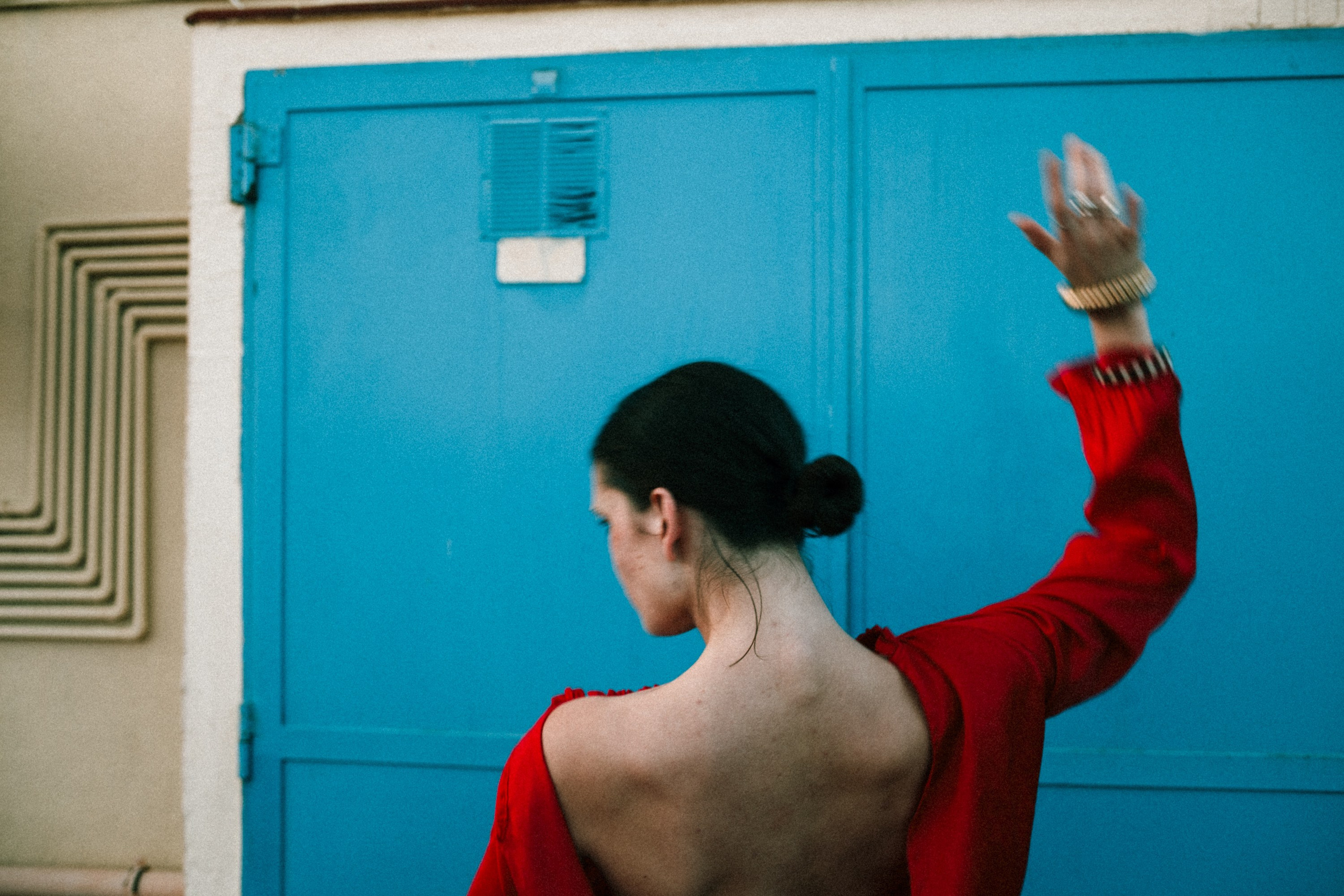 portrait of a woman in red dress from behind with raised arm, blue door background, Barcelona photographer