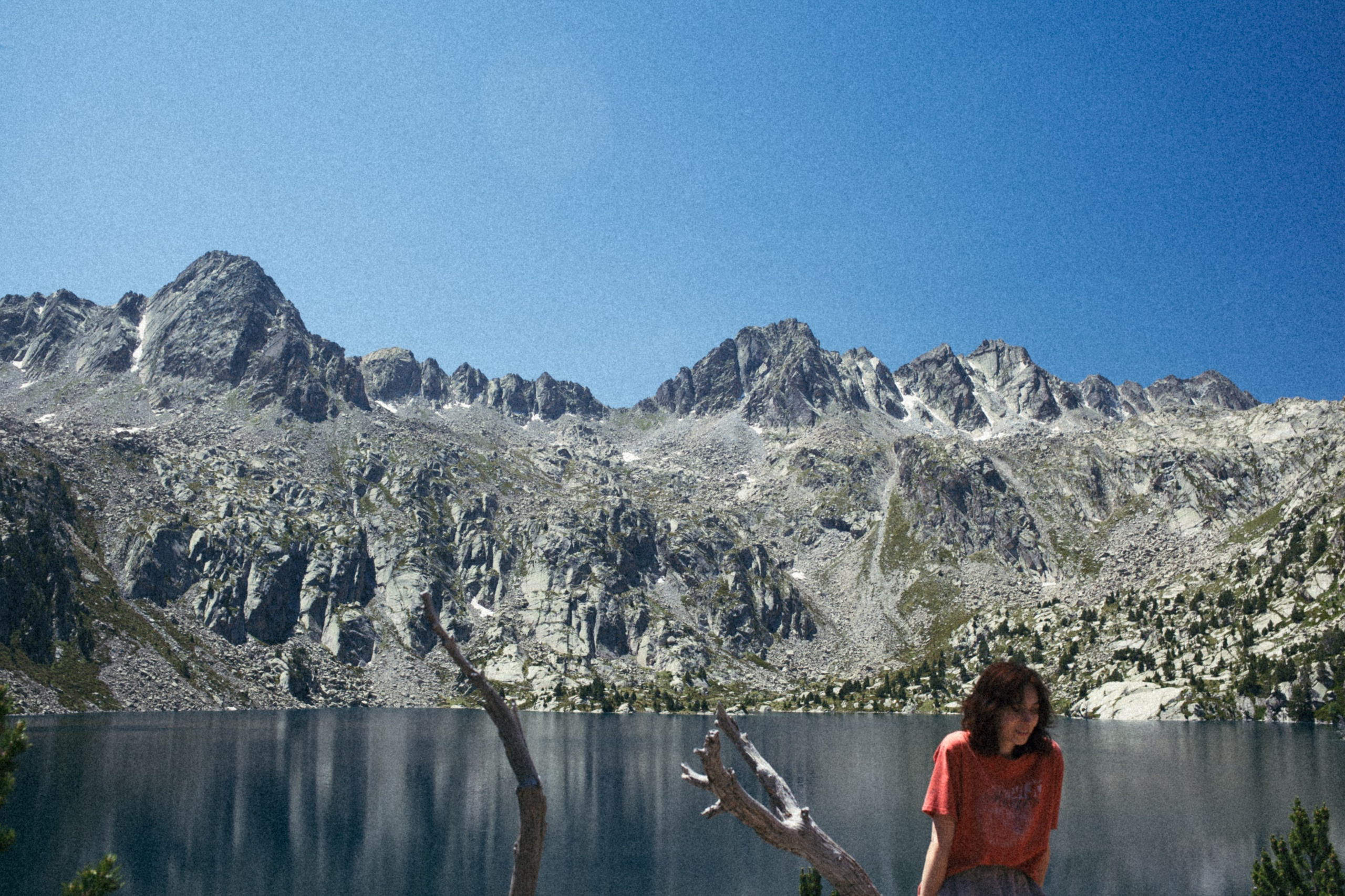 A female photographer standing in front of a mountain landscape, holding a camera, with a calm and focused expression