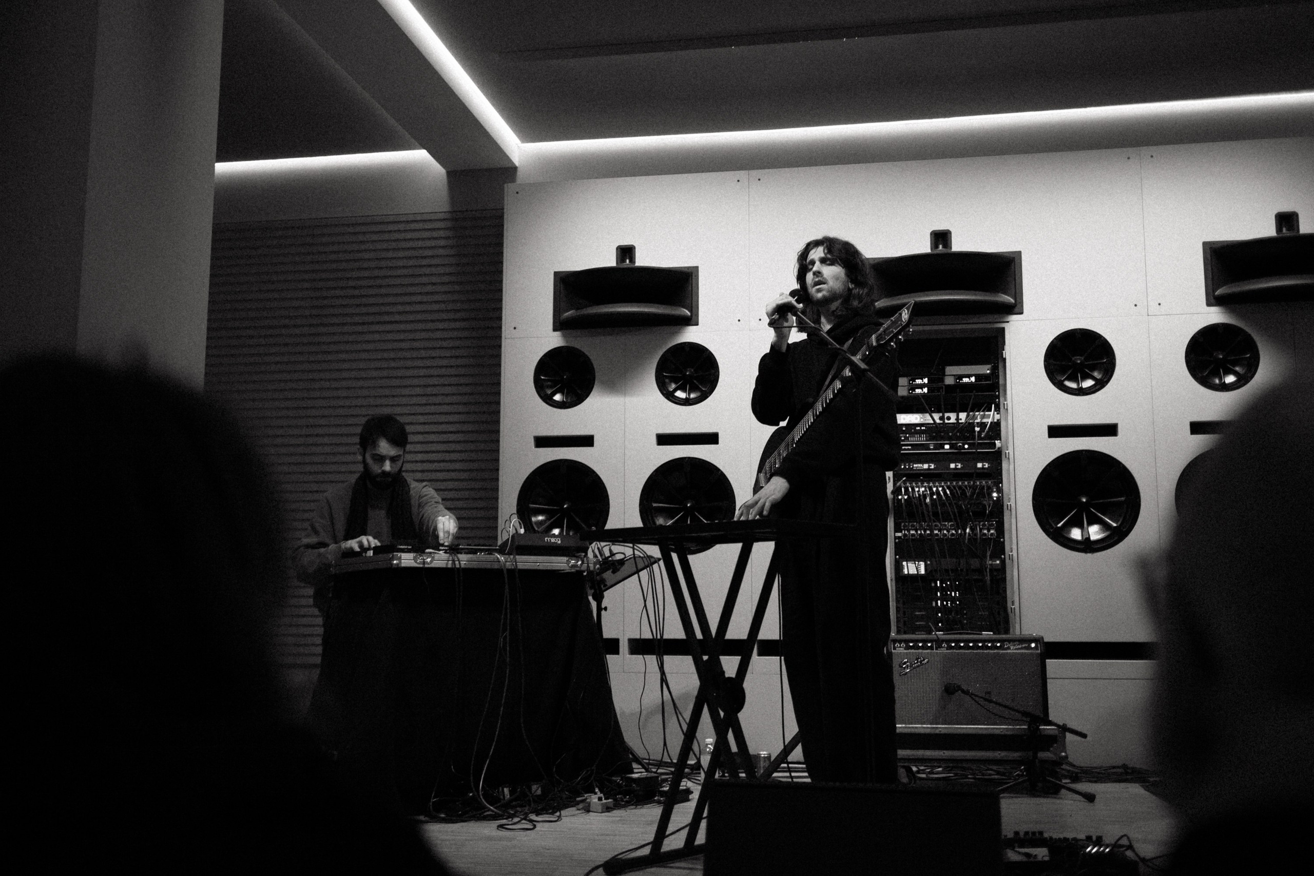 Live band performance, black and white — singer with guitar and pedal steel player on stage with studio monitors