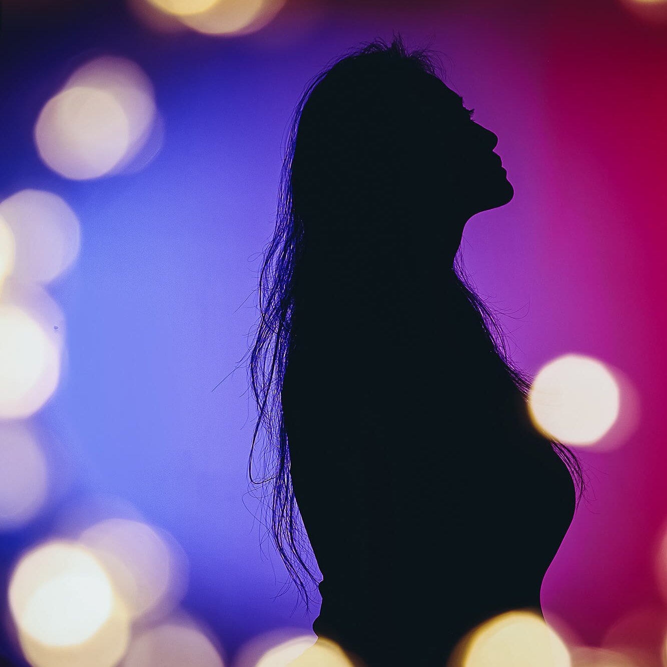 A striking silhouette of a woman against a gradient background of deep blue and magenta, surrounded by soft golden bokeh lights. Her posture, with her head tilted upward, conveys a sense of strength, confidence, and inner peace. The image symbolizes empowerment, self-reflection, and embracing personal growth.