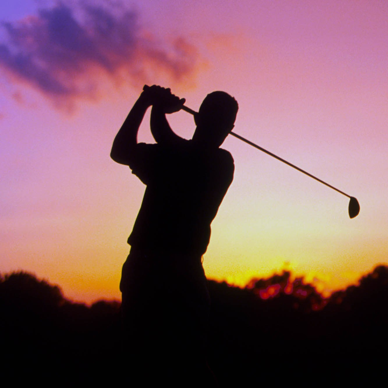 A golfer tees off on the fairway as the setting sun casts its vibrant hues across the landscape during a charity golfing event.