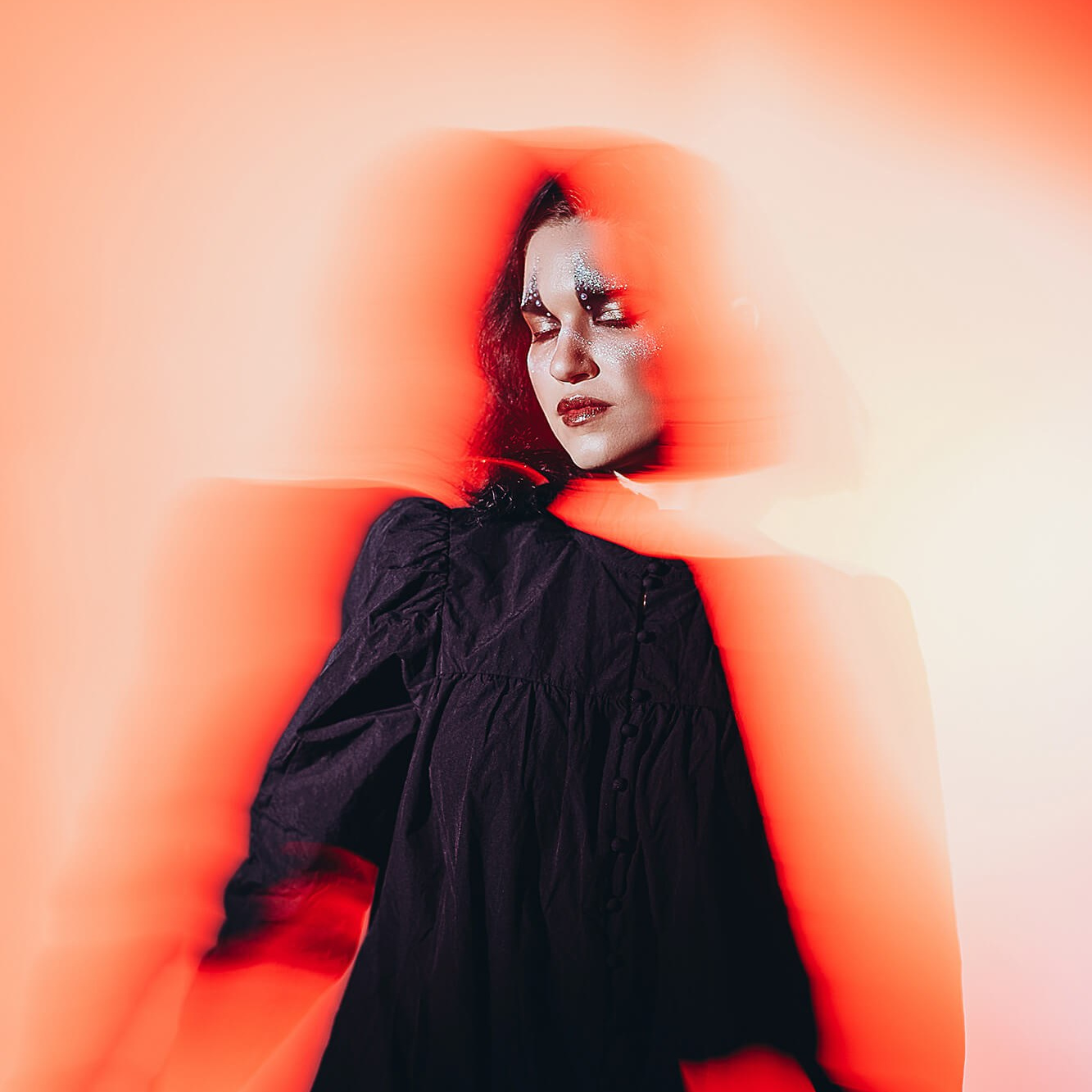 A powerful and artistic portrait of a woman in a black dress, surrounded by surreal red light trails. Her eyes are closed, and her face is adorned with shimmering silver makeup, symbolizing self-expression, transformation, and inner strength. The image evokes themes of empowerment, personal growth, and embracing one's unique identity.