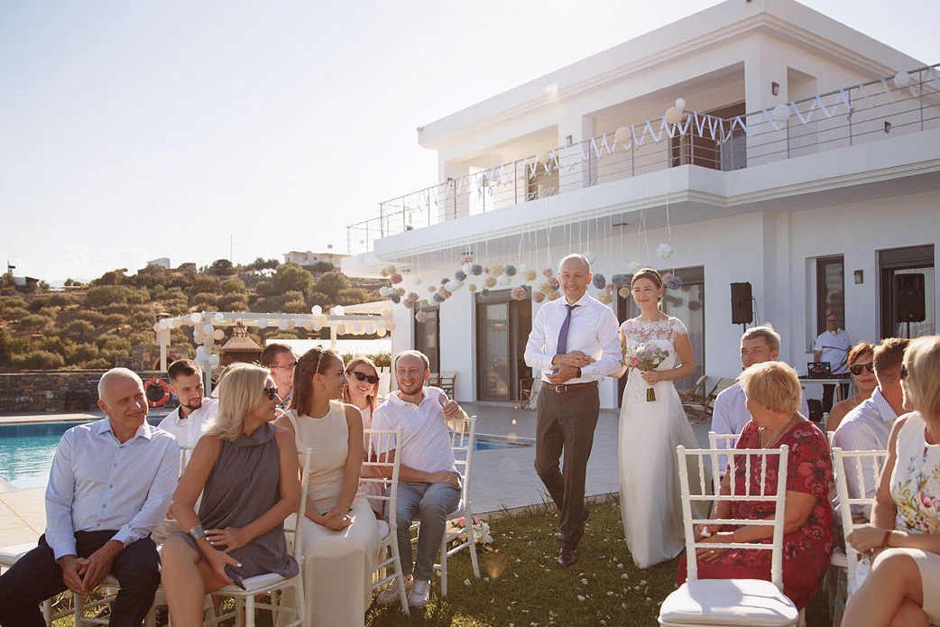 Отец ведет невесту к алтарю на свадебной церемонии на Крите. Фотограф, свадьба в Греции.