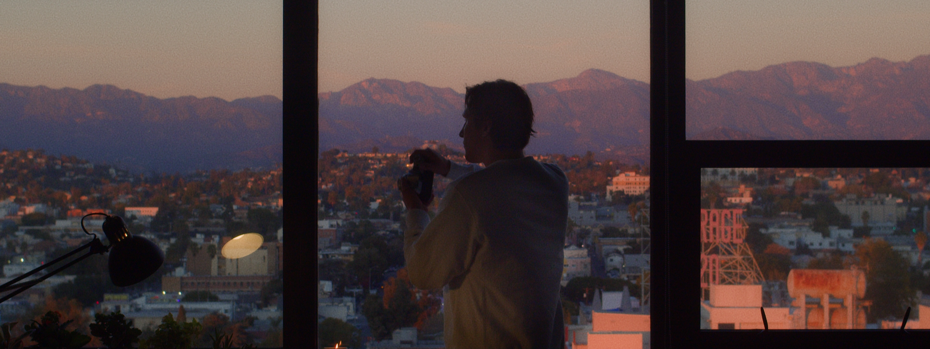 Breathtaking view of the Los Angeles skyline during sunset, captured through a large window, showcasing the city's iconic urban beauty.
