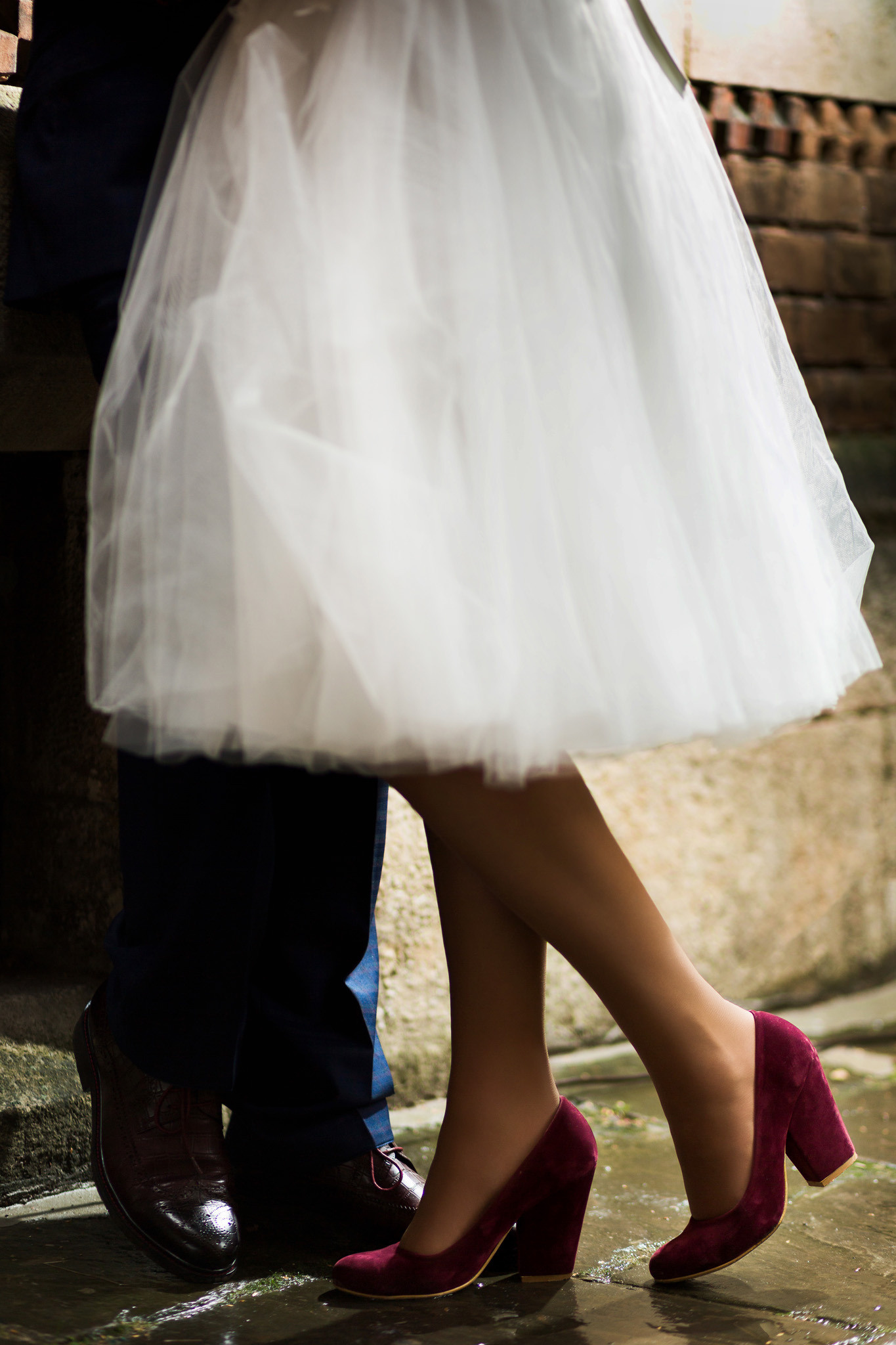 ножки наречених, наречений в темно синіх брюках і в туфлях, наречена в білому платті трошки нижче коліна в замшових червоних туфлях