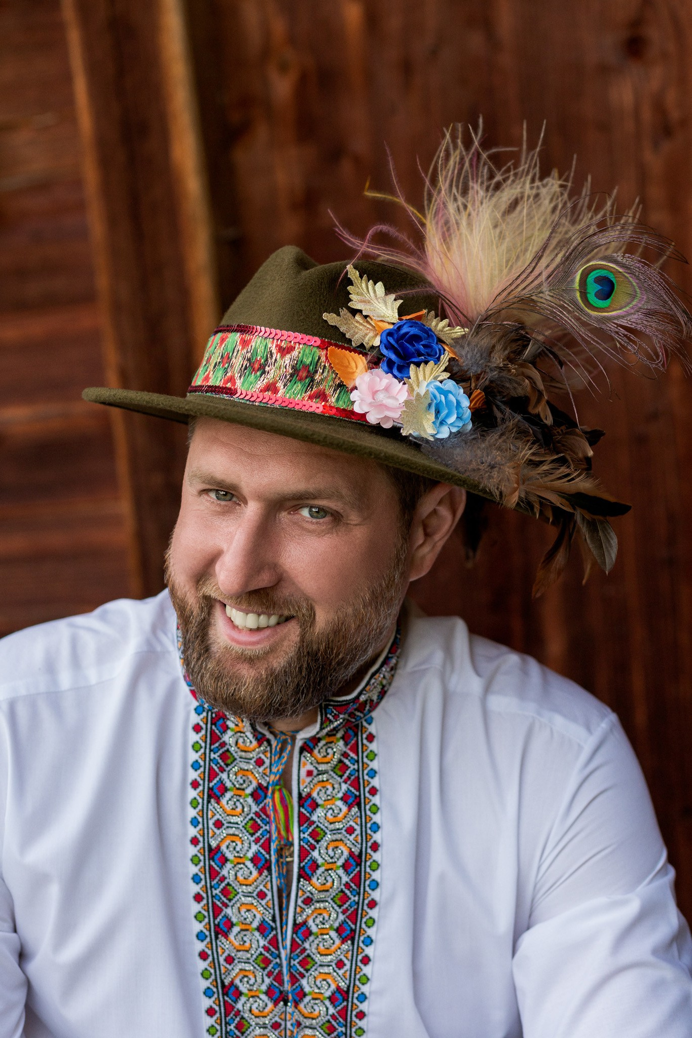 на фотографії зображена людина в національному вбранні і капелюхі, на якому розташовані квіти і перо павича