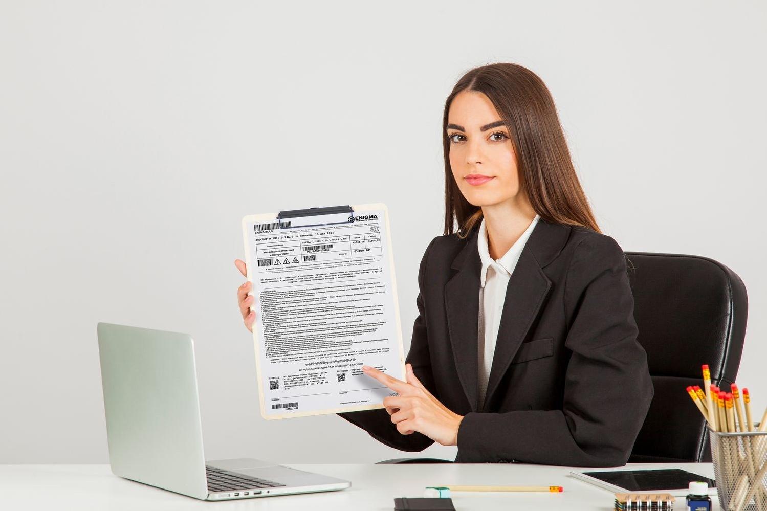Девушка за столом в офисе показывает образец договора по установке пластиковых окон с фирмой Enigma.