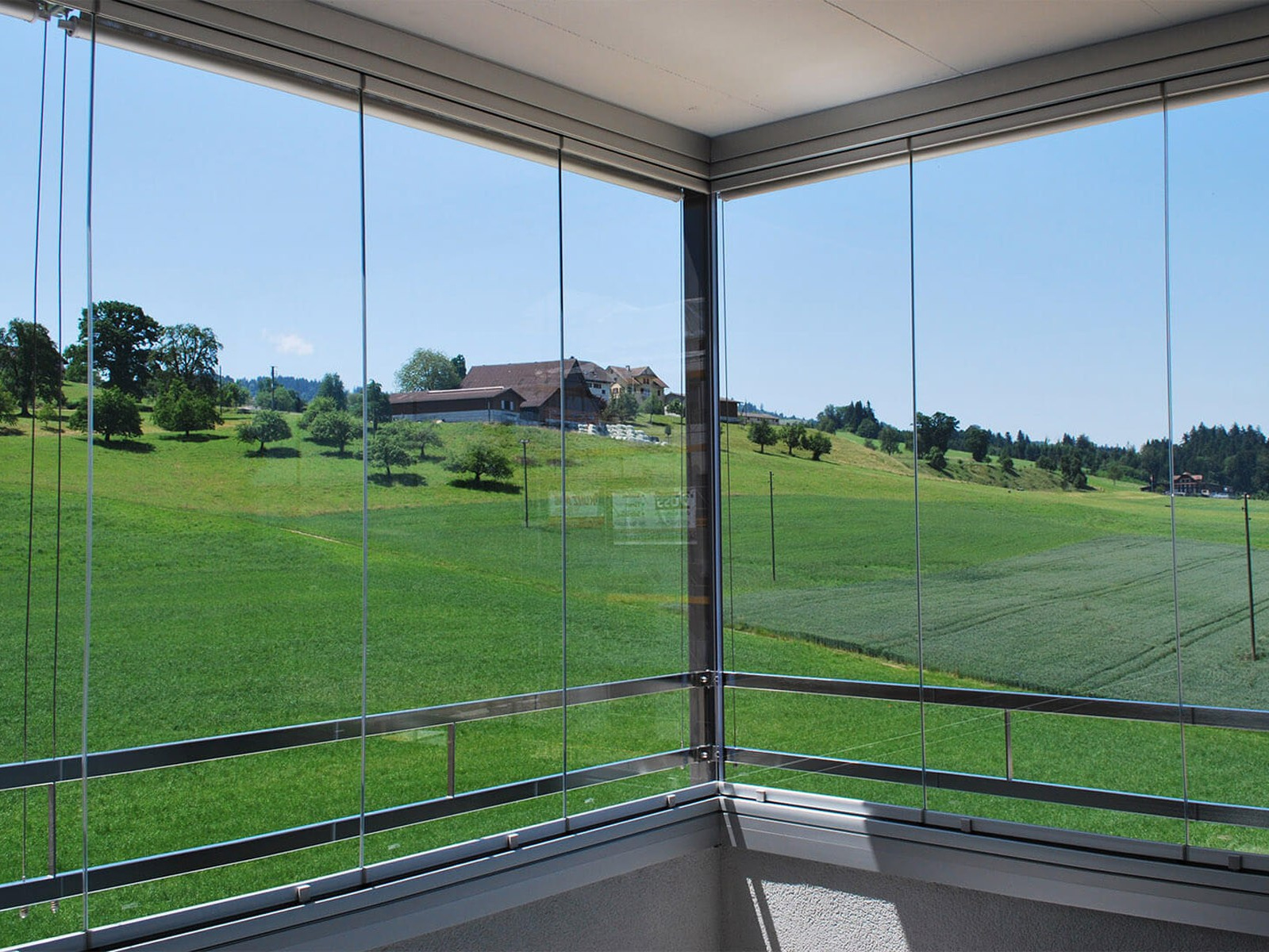 Безрамное остекление выполненное на террасе частного дома с видом на зеленый луг.