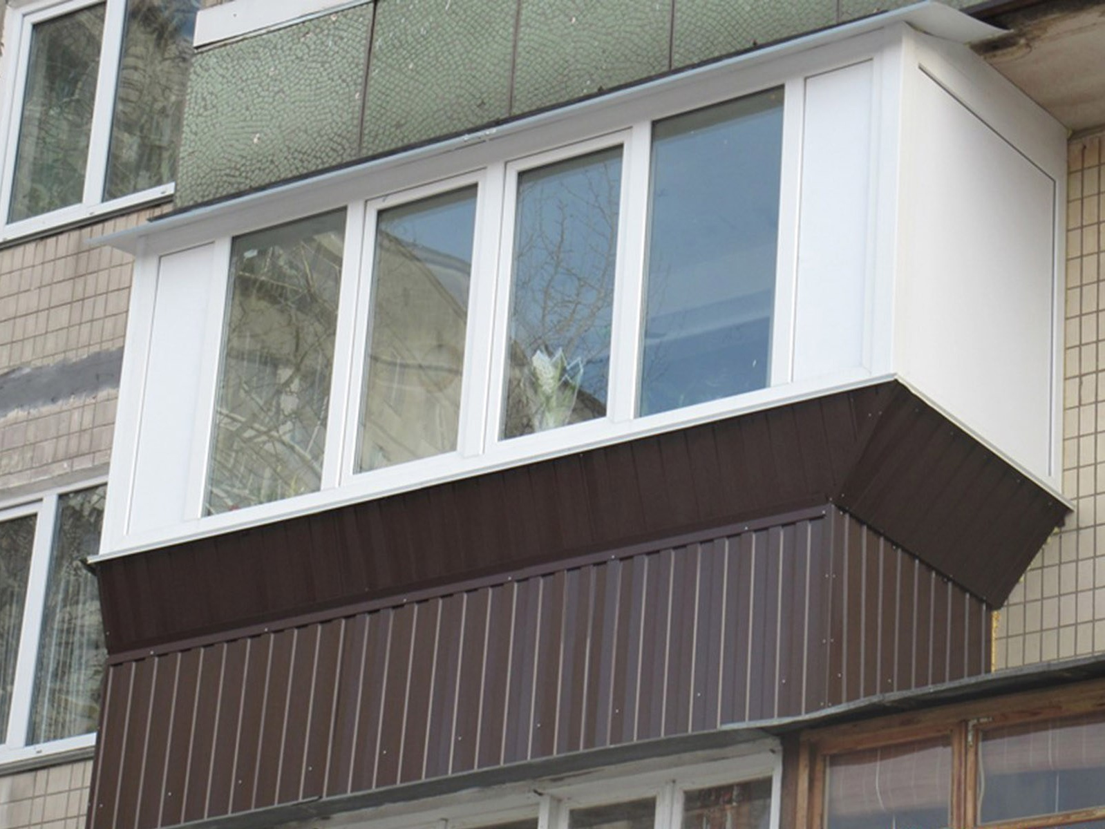 Пластиковый балкон белого цвета, с выносом рамы на 30см за габариты плиты в верхней части и обшитый сайдингом коричневого цвета - в нижней, по бокам закрыт сендвичем.