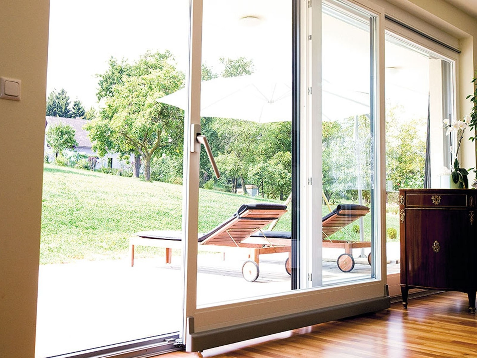 Комната с установленной металлопластиковой наклонно-раздвижной системой белого цвета с видом на летнюю террасу.