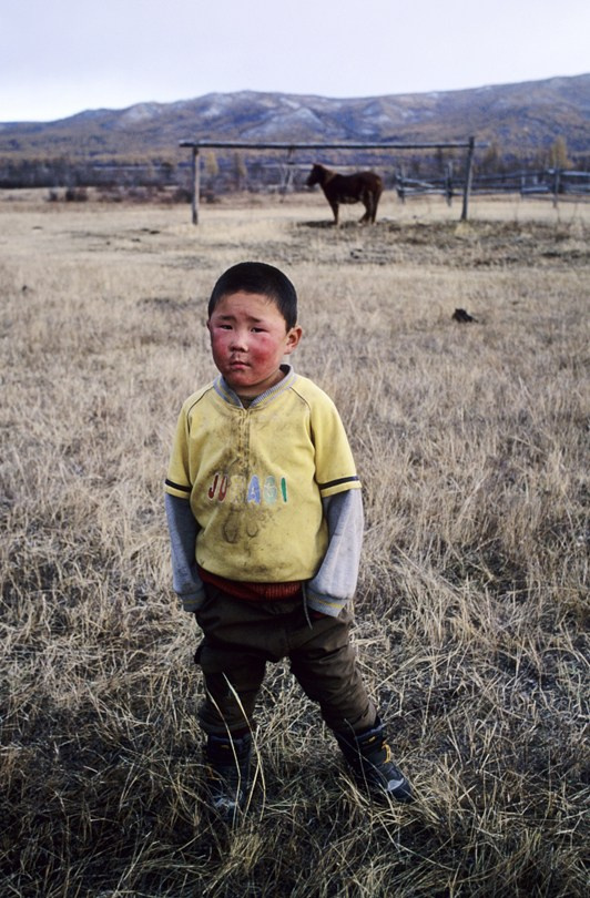 Portrait of a boy against the backdrop of a steppe landscape with a horse, Tsagaan-Üür district, Khövsgöl province, Mongolia. October 2010
