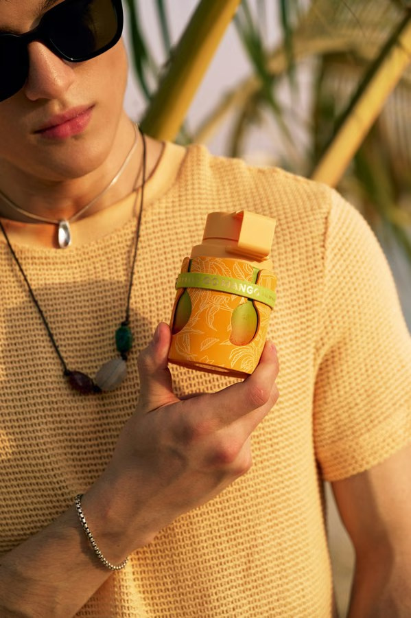 Lifestyle product photo of a mango-inspired perfume held by a model in warm light