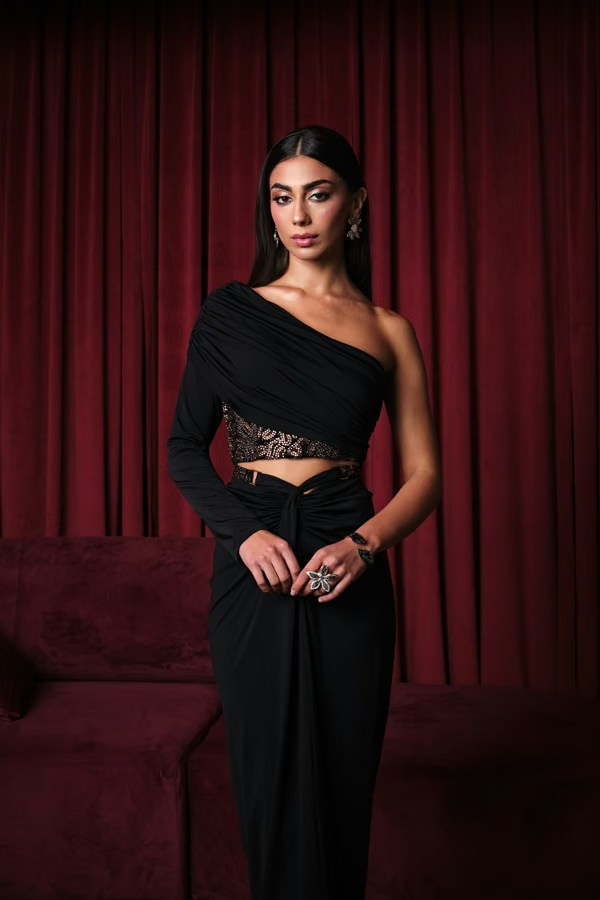Woman in formal black attire posed against deep red drapery