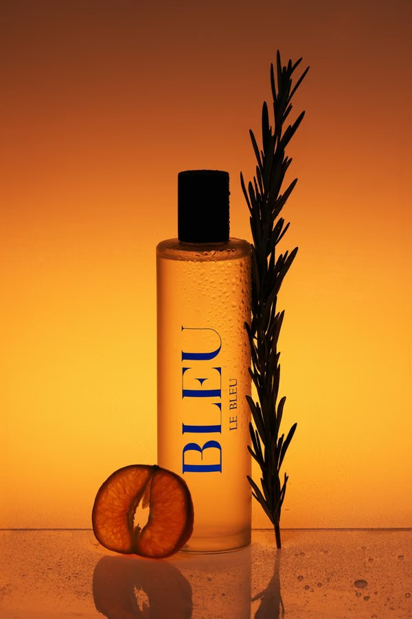 Amber perfume bottle with rosemary and orange slices on a warm orange background