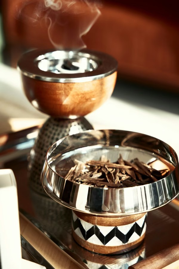 Metallic bakhoor burner filled with oud chips and rising incense smoke