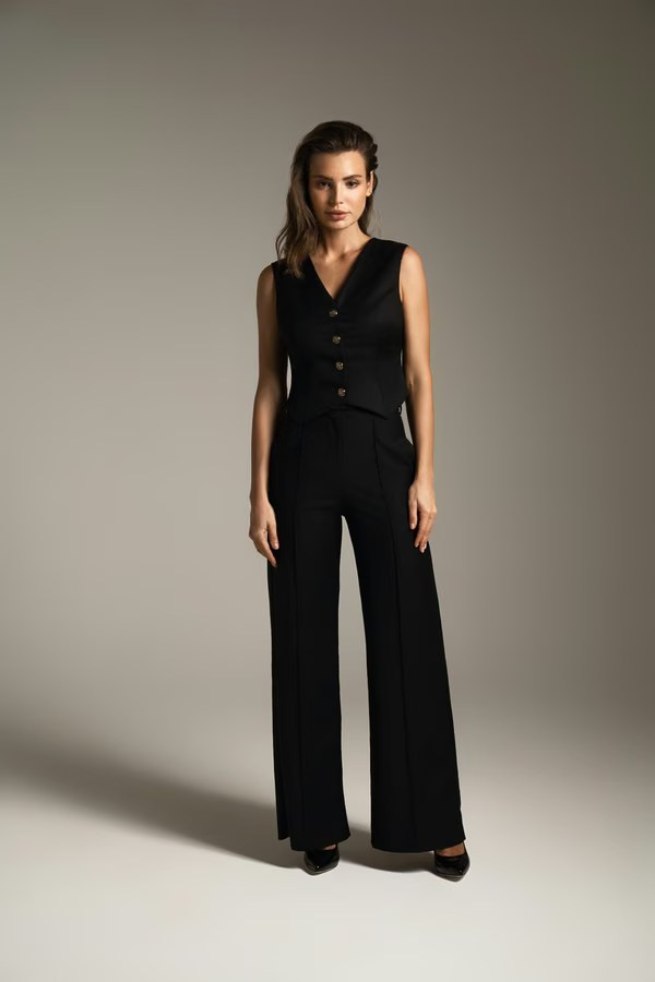 Woman wearing a black tailored vest and wide-leg trousers against a neutral background