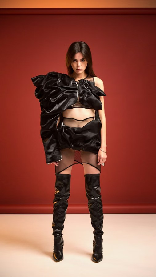 Woman in an avant-garde black outfit with exaggerated shoulders against a red background