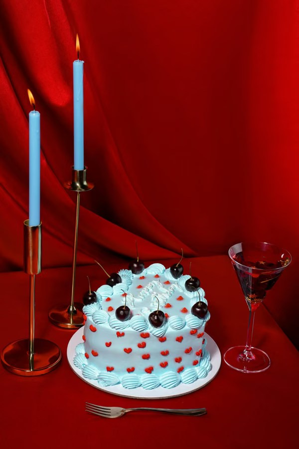 Blue iced cherry cake with red candles on a red tabletop