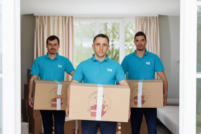 Trois employés portent des cartons dans un salon lumineux