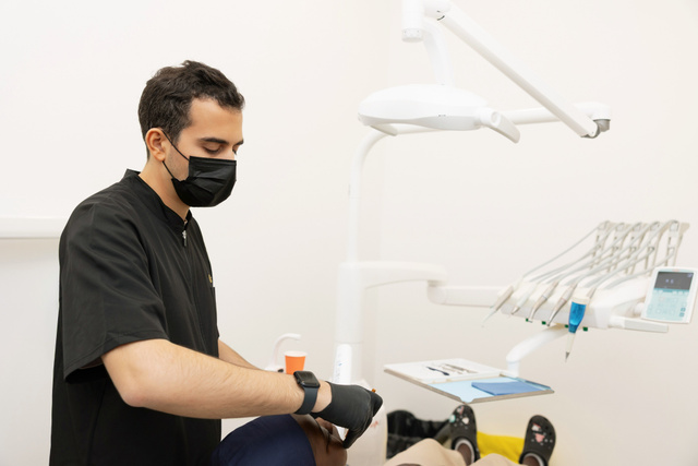 Le praticien au fauteuil avec un patient, visage du patient non visible