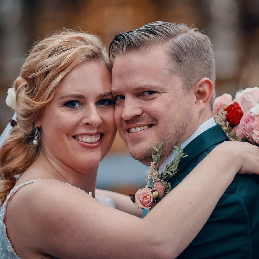 Red-haired bride holding her flowing veil aloft smiles seductively to her bouquet holding groom as he leans back against a railing in appreciation at the Vrtba Garden in Prague. 