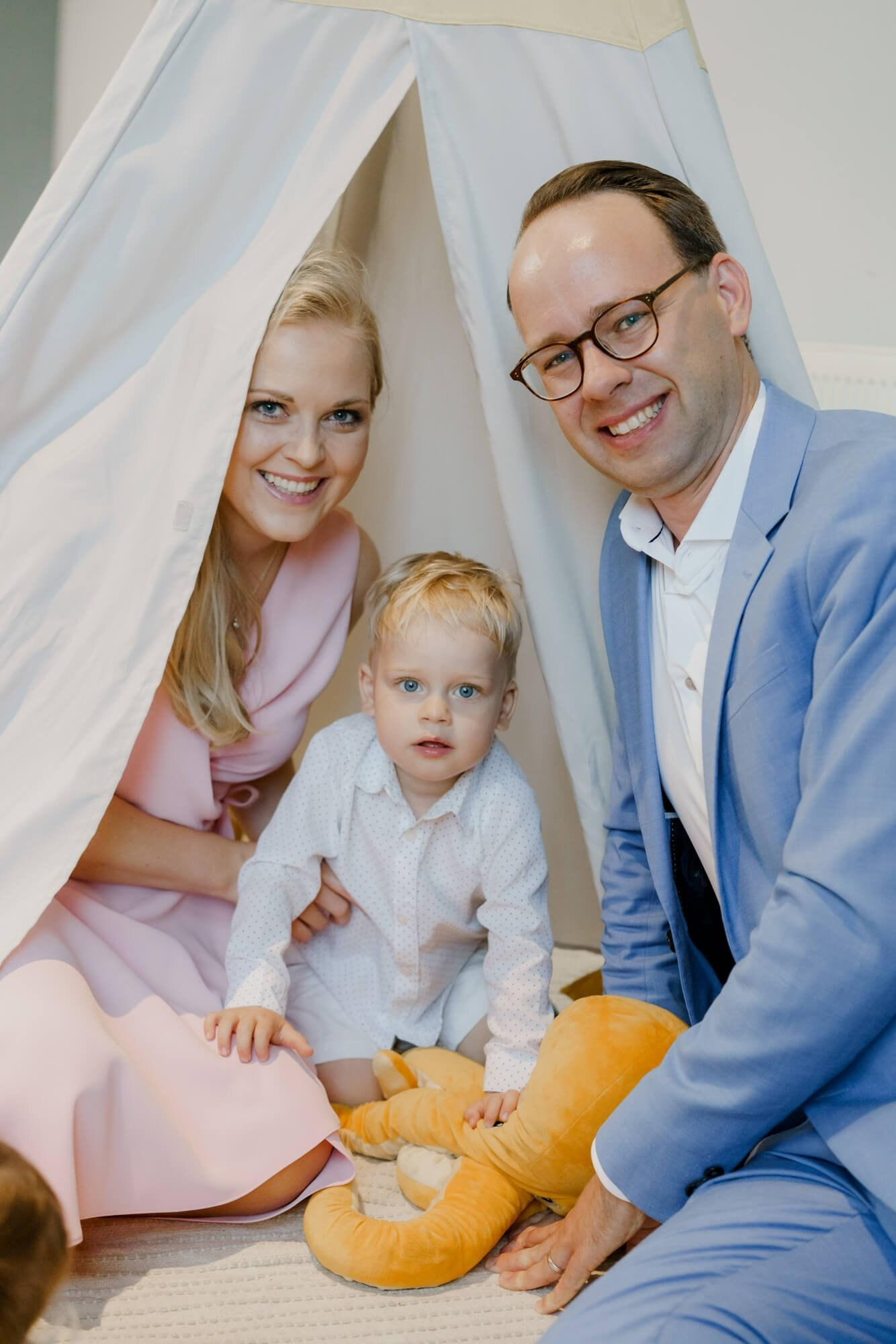 Two wedding guests posing with a toddler inside a small white play tent set up for children at the reception