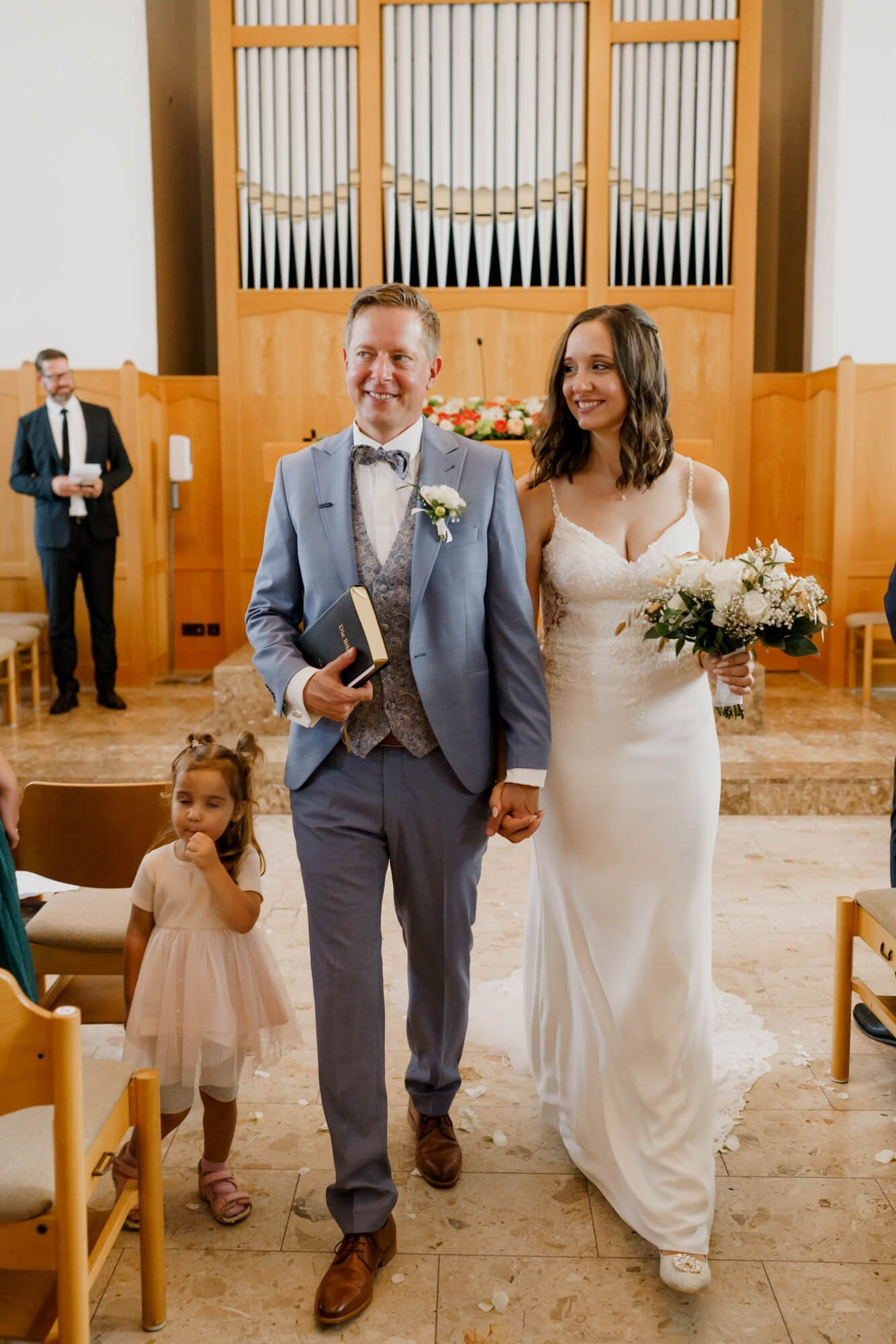 Couple walking back down the aisle together after the wedding ceremony in Stuttgart, both smiling, pipe organ visible at the rear