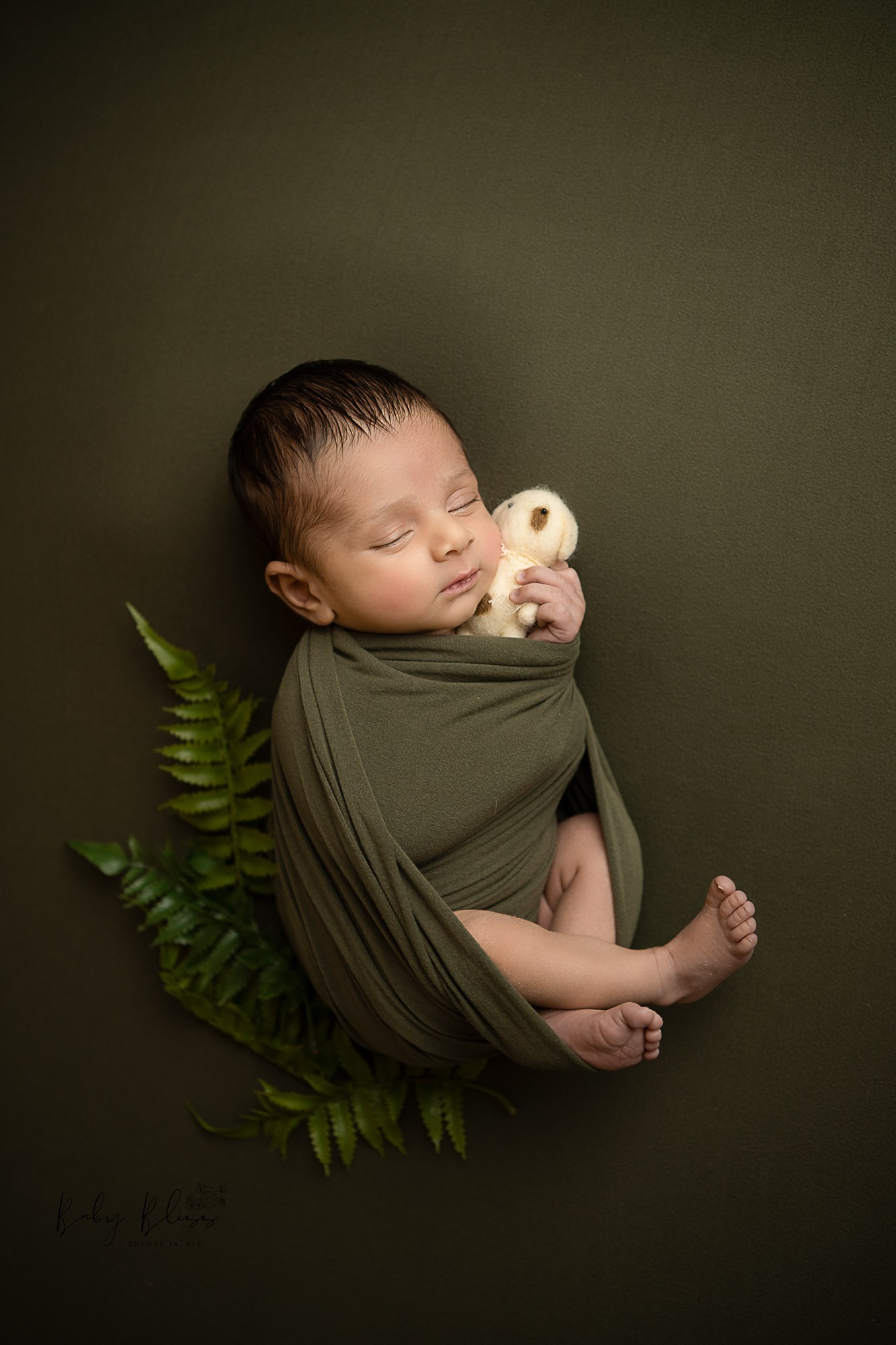 newborn baby sleeping peacefully holding a toy in a olive green colour wrap for newborn photo shoot.