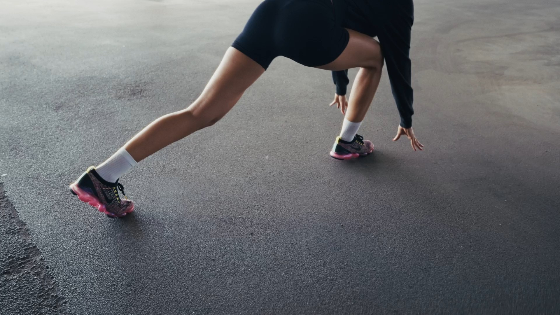 A dynamic low-angle shot of a person stretching one leg forward on an urban surface, with an athletic and focused pose.