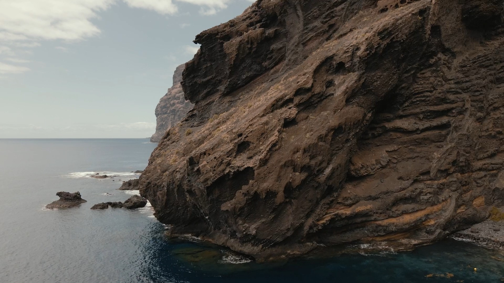 A rugged coastal cliff of Los gigantes, Tenerife plunging into clear blue waters, showcasing dramatic textures of the rock formation against a serene ocean backdrop.