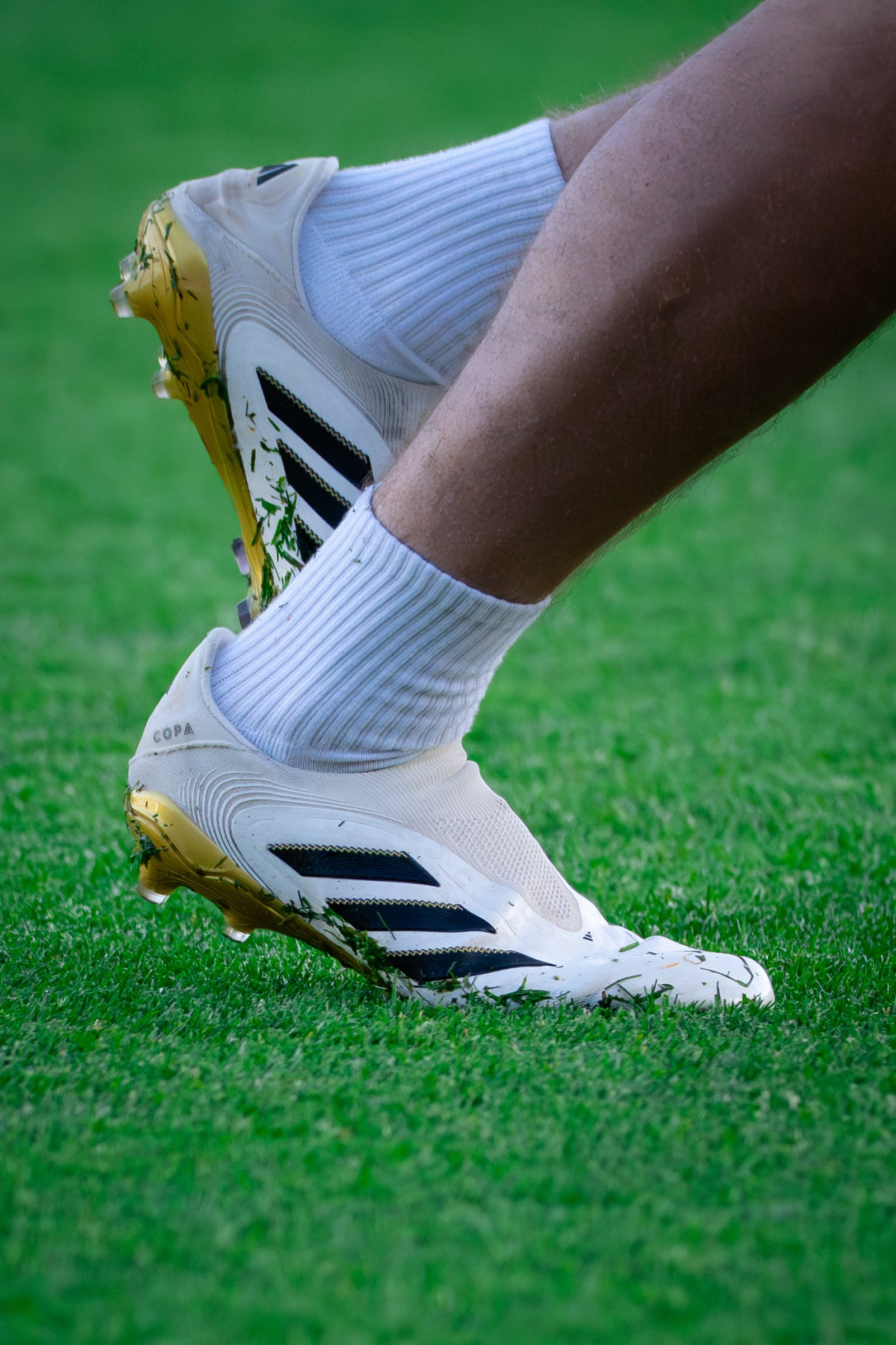Close-up of a professional football player’s boots and white socks on the pitch.