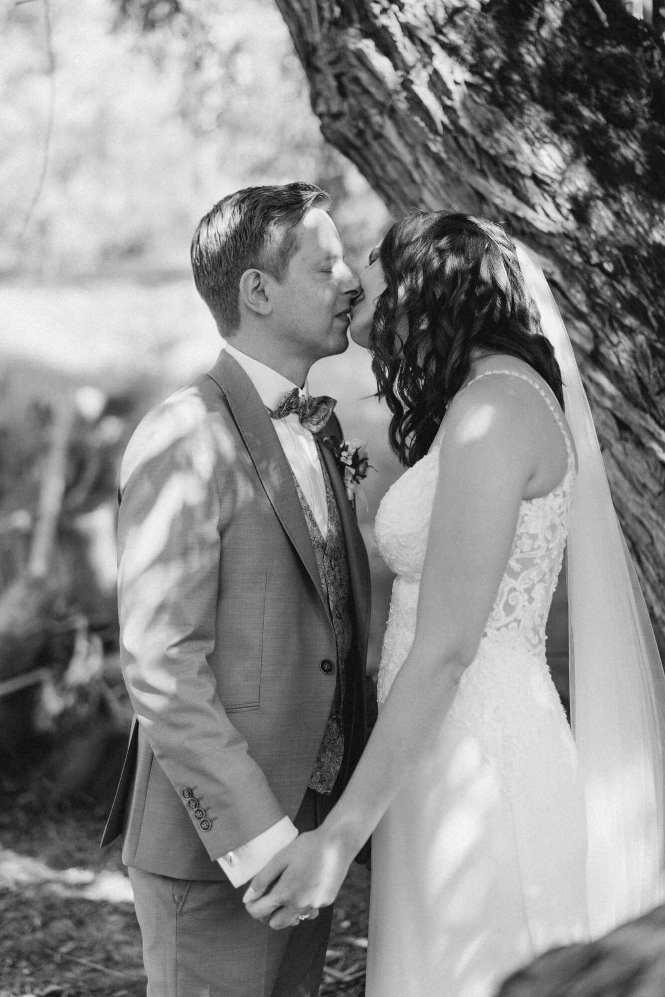 Couple leaning in for a kiss, hands clasped, the bride's veil softly framing the moment; black and white