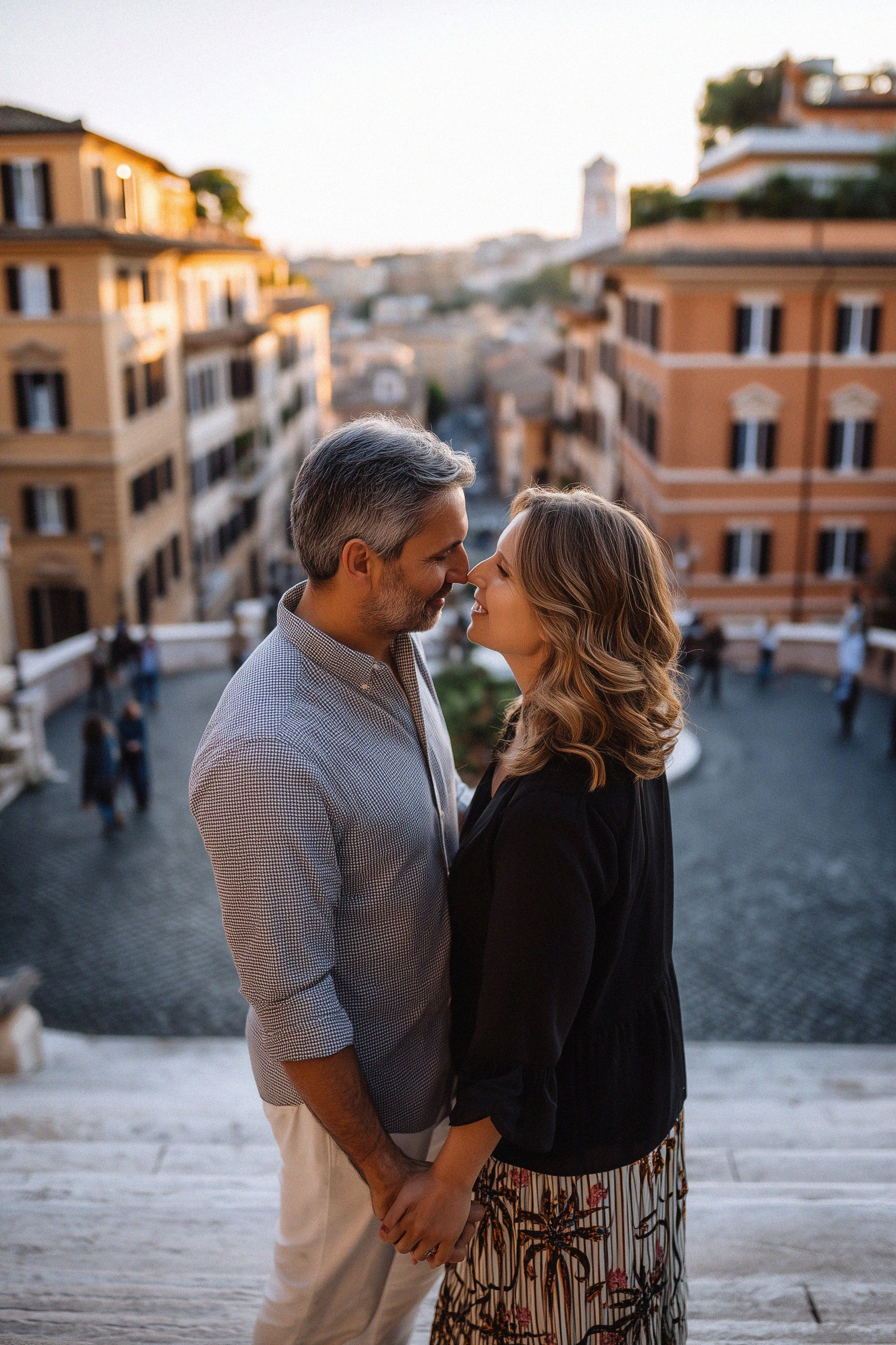 A couple stands on the Spanish Steps at sunset, leaning in for a kiss with the rooftops of Rome behind them.
