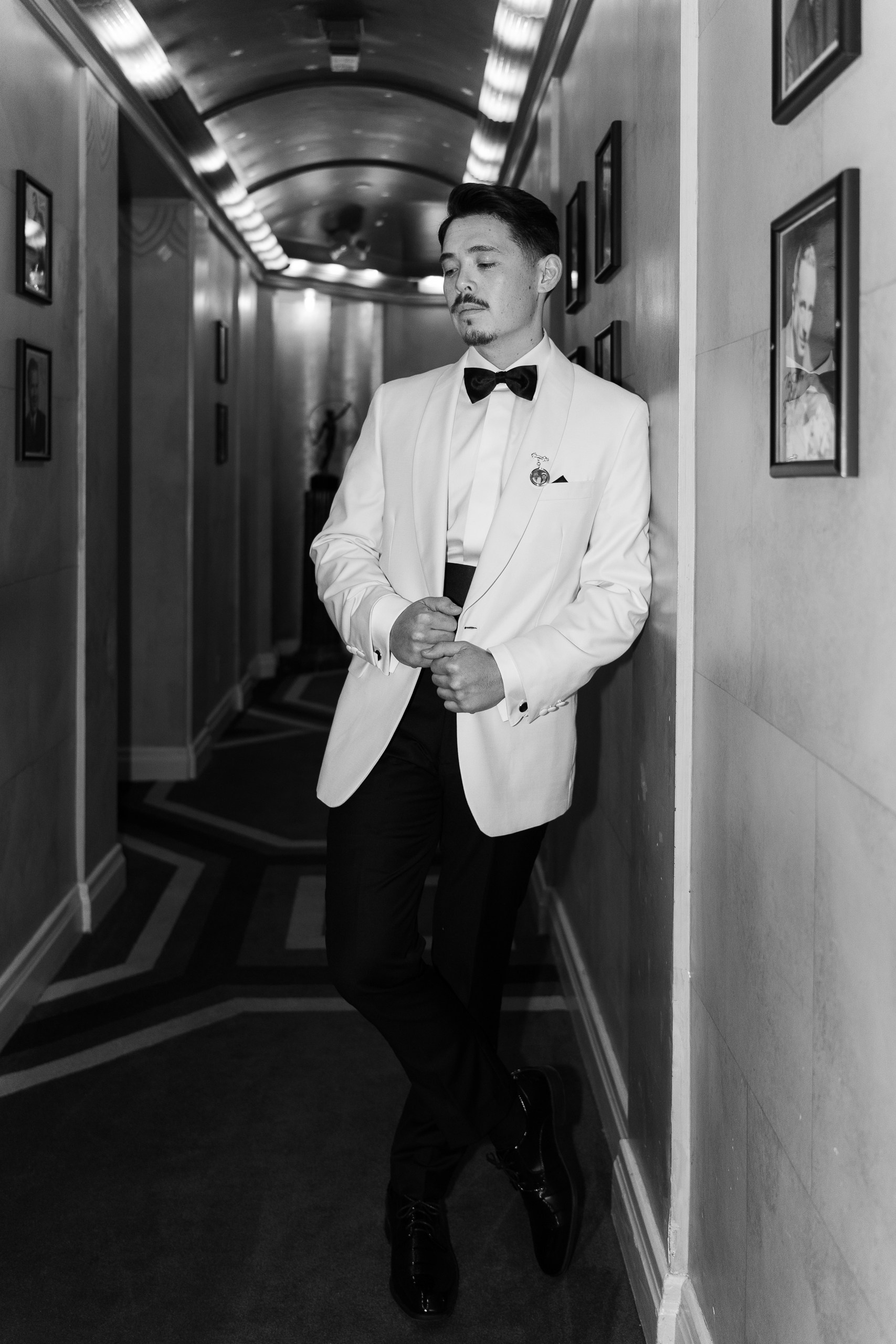 Groom wearing stylish white tuxedo with black bow tie 